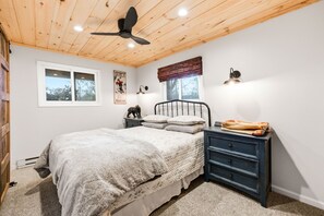 A bedroom with a bed, a nightstand, a dresser, a ceiling fan, a window, and a wall-mounted lamp. - Glass Peak Cabin - Panoramic Mountain Views - Hot Tub - Sugar Mountain (Sugar Mountain)