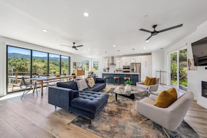 A spacious living area with a large sofa, a coffee table, and a dining area with a view of the outdoors.