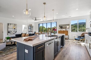 A modern kitchen with a large island, pendant lighting, and a view of the outdoors. - The Vintara - Glen Ellen,Hot Tub, New Construction (Glen Ellen)