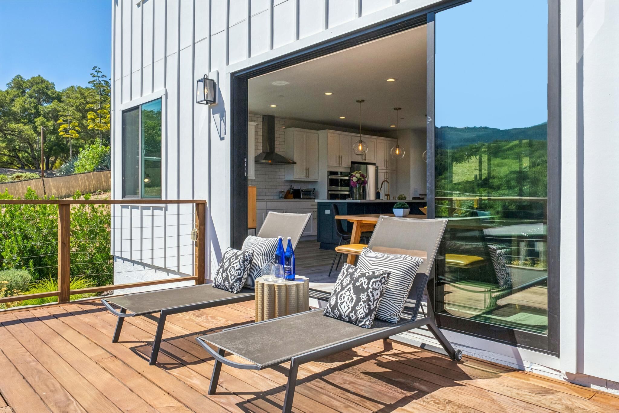 Eine moderne Terrassenausstattung mit Liegestühlen und Tisch, eine Glastür, die zur Küche führt, und Blick ins Grüne.