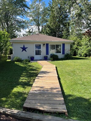 A single-story house with a front porch, a star decoration, and a wooden pathway leading to the entrance. - Cozy Cottage Retreat on Jordan Lake with Amazing Views and Great Fishing (Lake Odessa)