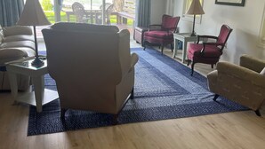 Ein Wohnzimmer mit einer Couch, Sesseln, einem Couchtisch, einem Fernseher und Blick ins Freie.