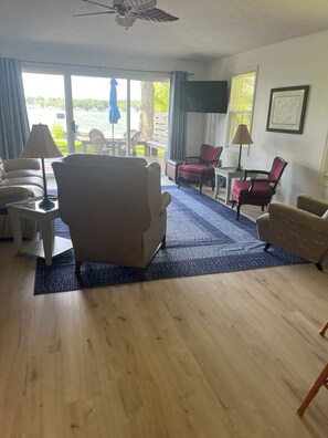 A living room with a sofa, armchairs, a coffee table, a TV, and a view of the outdoors. - Cozy Cottage Retreat on Jordan Lake with Amazing Views and Great Fishing (Lake Odessa)