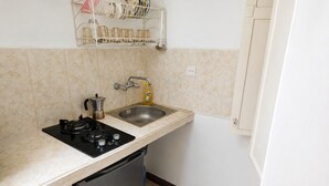 Een keuken met een gasfornuis, spoelbak en een plank boven de spoelbak met servies en potten.