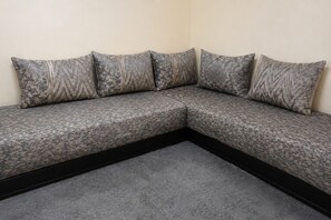 A sectional sofa with a patterned fabric and a dark frame, positioned against a plain wall. - Dar El Medina (Casablanca)