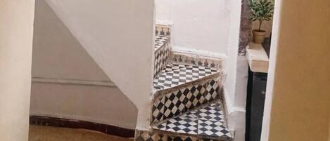 A narrow stairway with a checkered floor leading to a room with a window.