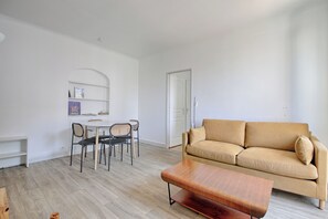 Ein Wohnzimmer mit einem beigefarbenen Sofa, einem Holztisch, einem Esstisch mit Stühlen und einer weißen Tür.
