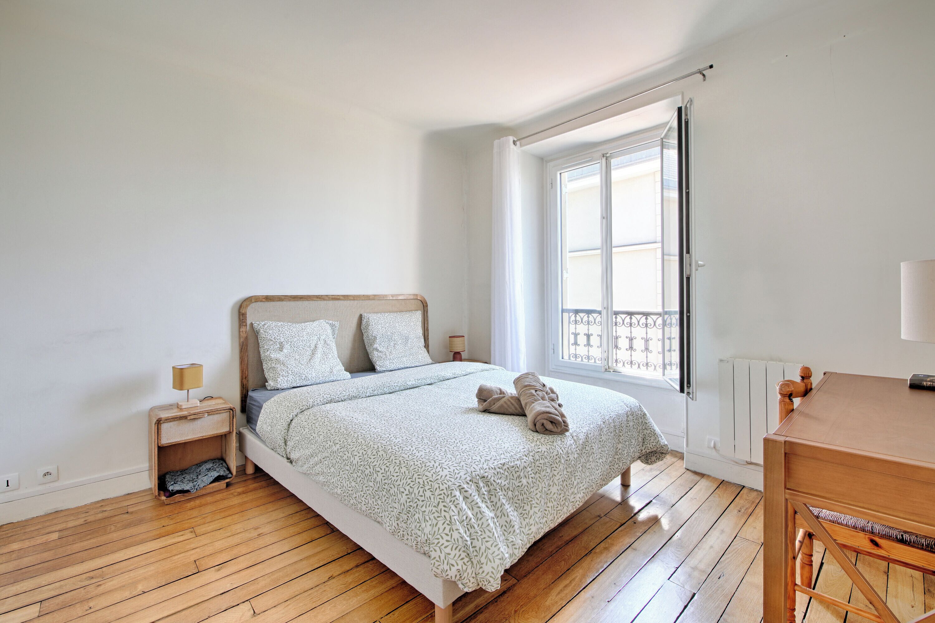 A bedroom with a wooden bed, a nightstand, a window with a view, and a wooden table.
