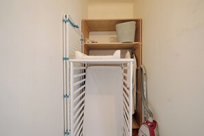 Ein kleiner, abgeschlossener Raum mit einem weißen Metallkinderbett, einem Regal mit einem Korb und einem Staubsauger.