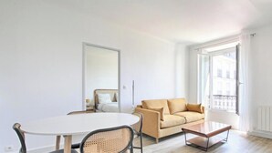 Quarto com uma mesa de jantar redonda, um sofá, uma cama e uma janela grande com cortinas.