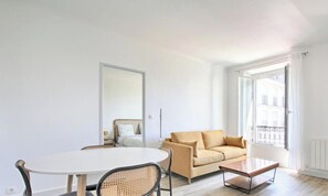 Ein Zimmer mit einem runden Esstisch, einer Couch, einem Bett und einem großen Fenster mit Vorhängen.