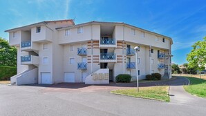 A multi-story residential building with balconies, a central entrance, and a parking area. - Le Scalby - Piscine - Golf (Pornic)