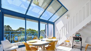 A modern dining area with a large table, yellow chairs, and a view through expansive windows. - Le Scalby - Piscine - Golf (Pornic)