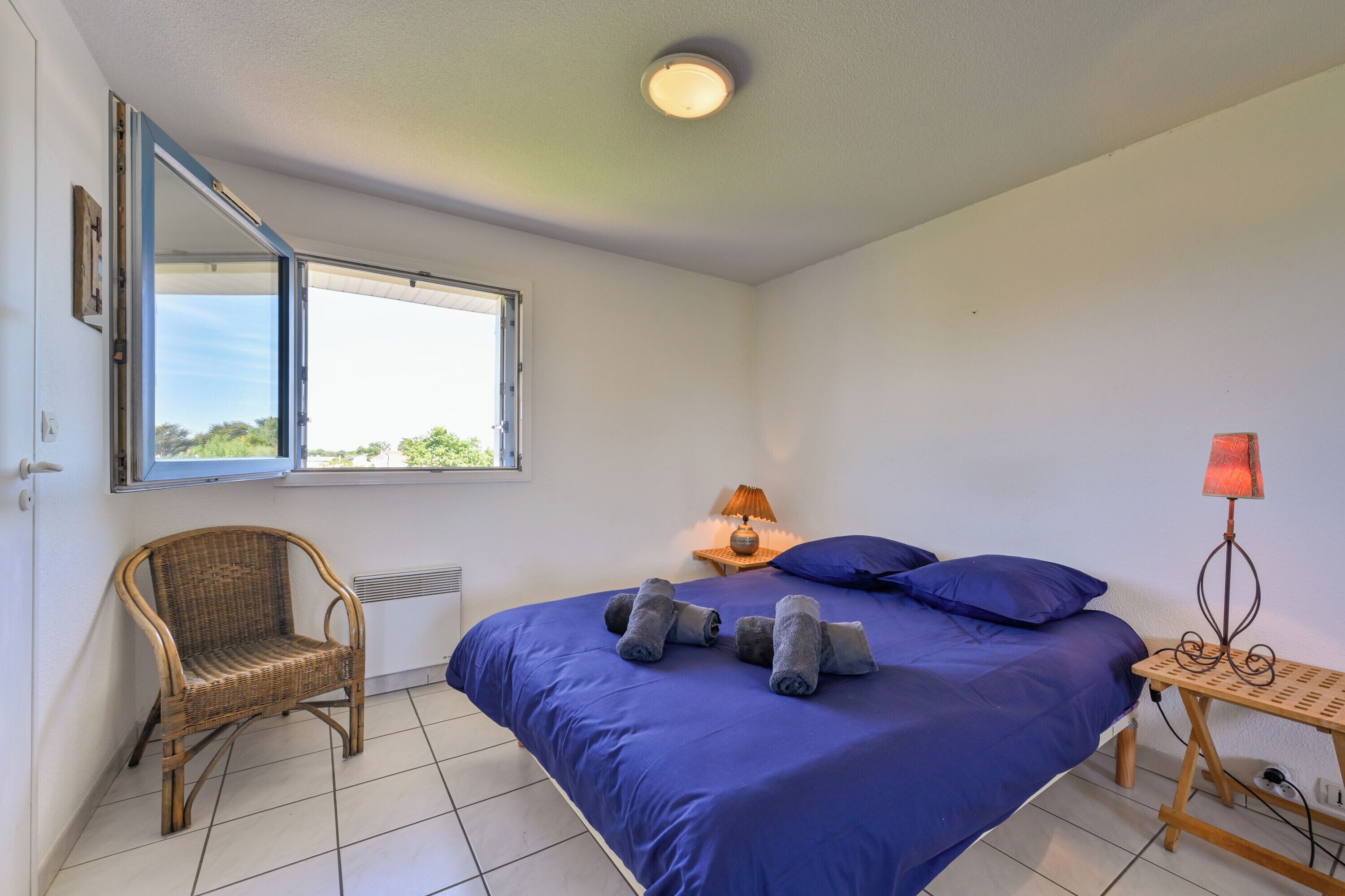 A bedroom with a bed, a chair, a nightstand, a lamp, and a window.