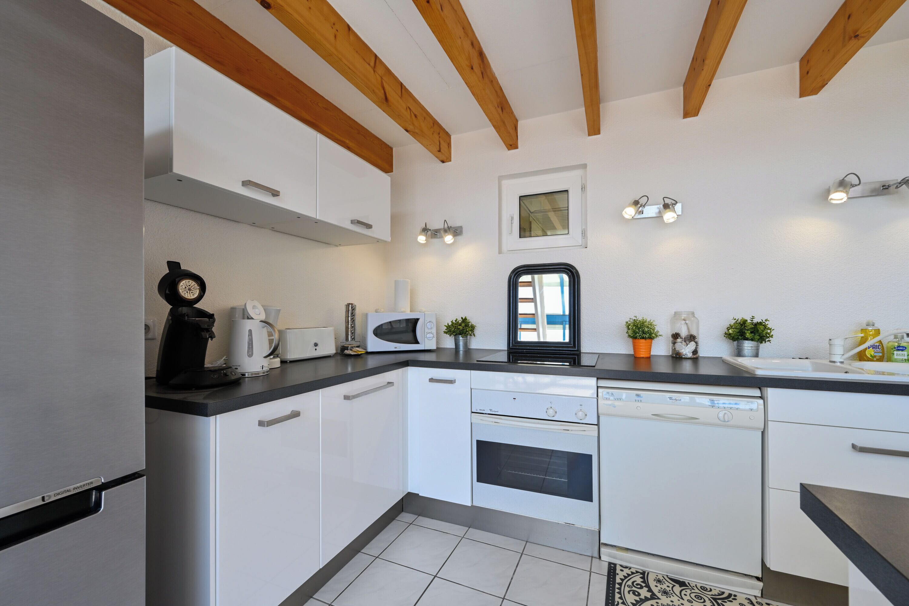A modern kitchen with white cabinets, a dishwasher, a microwave, and wooden beams on the ceiling.