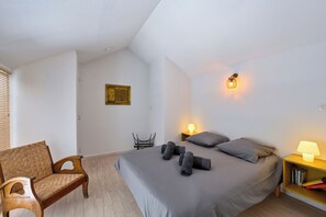 Ein Schlafzimmer mit einem Bett, einem Sessel, einem Nachttisch mit Lampe und einer Wandleuchte.