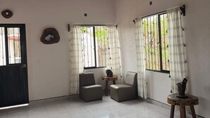 A spacious room with a tiled floor, two leather chairs, a small wooden table, a ceiling fan, and a window with curtains. - House near beautiful beaches. Separate entrance, with parking. Secure. (Las Varas)