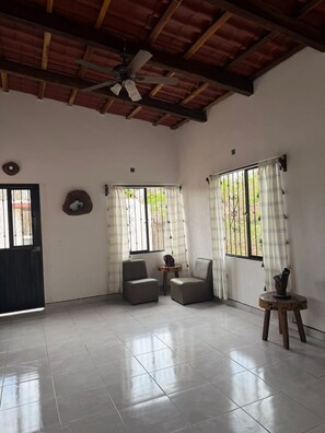 A spacious room with a tiled floor, two leather chairs, a small wooden table, a ceiling fan, and a window with curtains. - House near beautiful beaches. Separate entrance, with parking. Secure. (Las Varas)