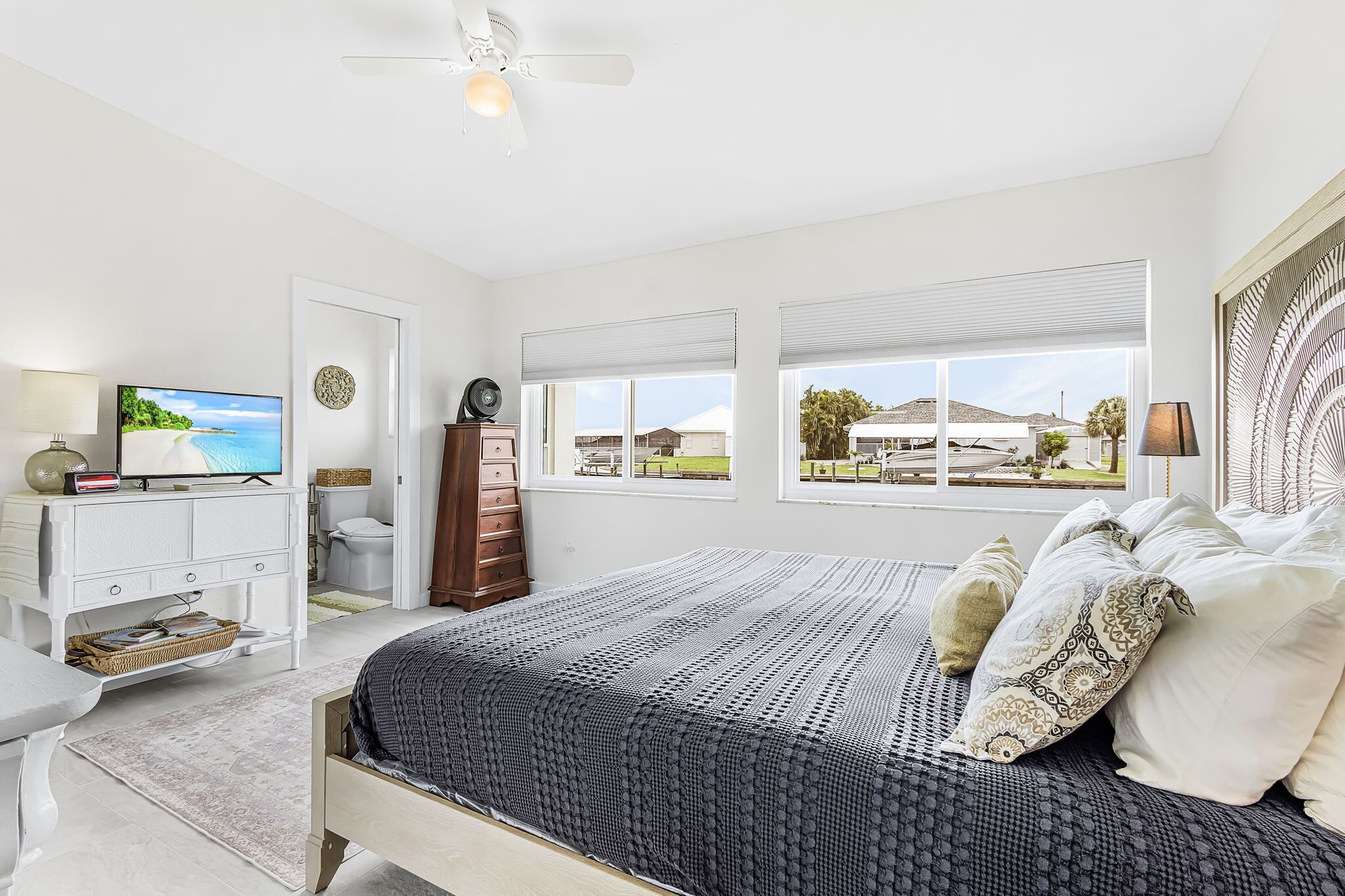 Un dormitorio con cama, televisión, cómoda, escritorio y vistas al exterior.