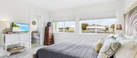 Un dormitorio con cama, televisión, cómoda, escritorio y vistas al exterior.