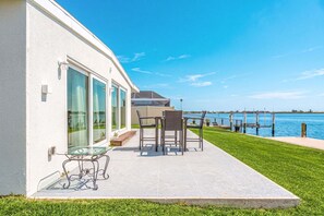 Une maison moderne dotée d’un patio donnant sur un plan d’eau, avec une table et des chaises en verre.