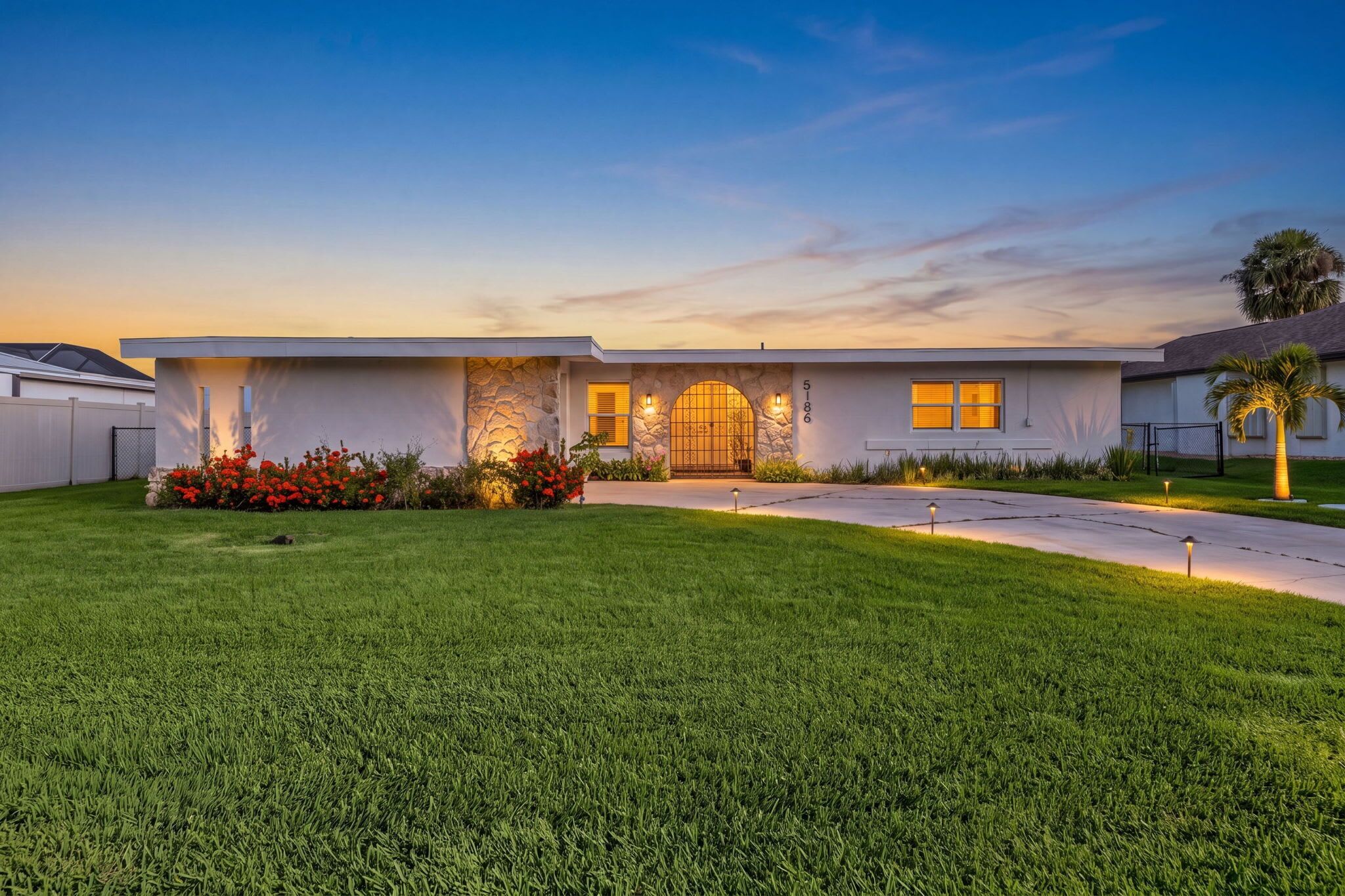 A modern two-story house with a stone facade, a large arched entrance, and a well-maintained lawn.