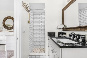 Une salle de bain avec des carreaux de céramique blancs rectangulaires, un lavabo sur plan de toilette noir et un miroir.