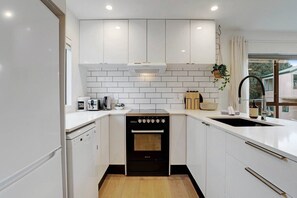 A compact kitchen with white cabinetry, a built-in oven, a dishwasher, and a sink with a modern faucet.