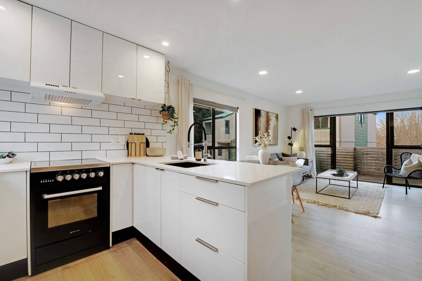 A modern kitchen with white cabinetry, a black stove, and a large window.