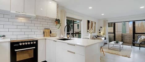 A modern kitchen with white cabinetry, a black stove, and a large window.