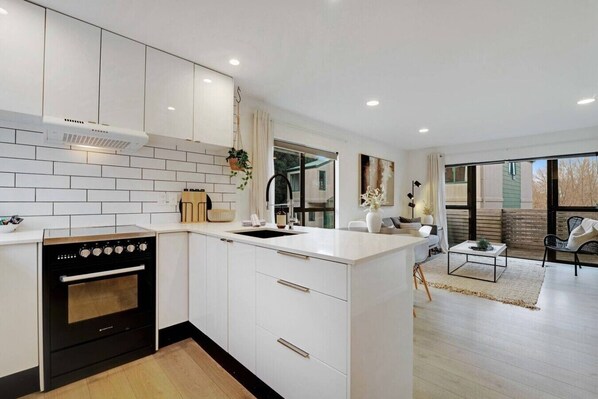 A modern kitchen with white cabinetry, a black stove, and a large window.