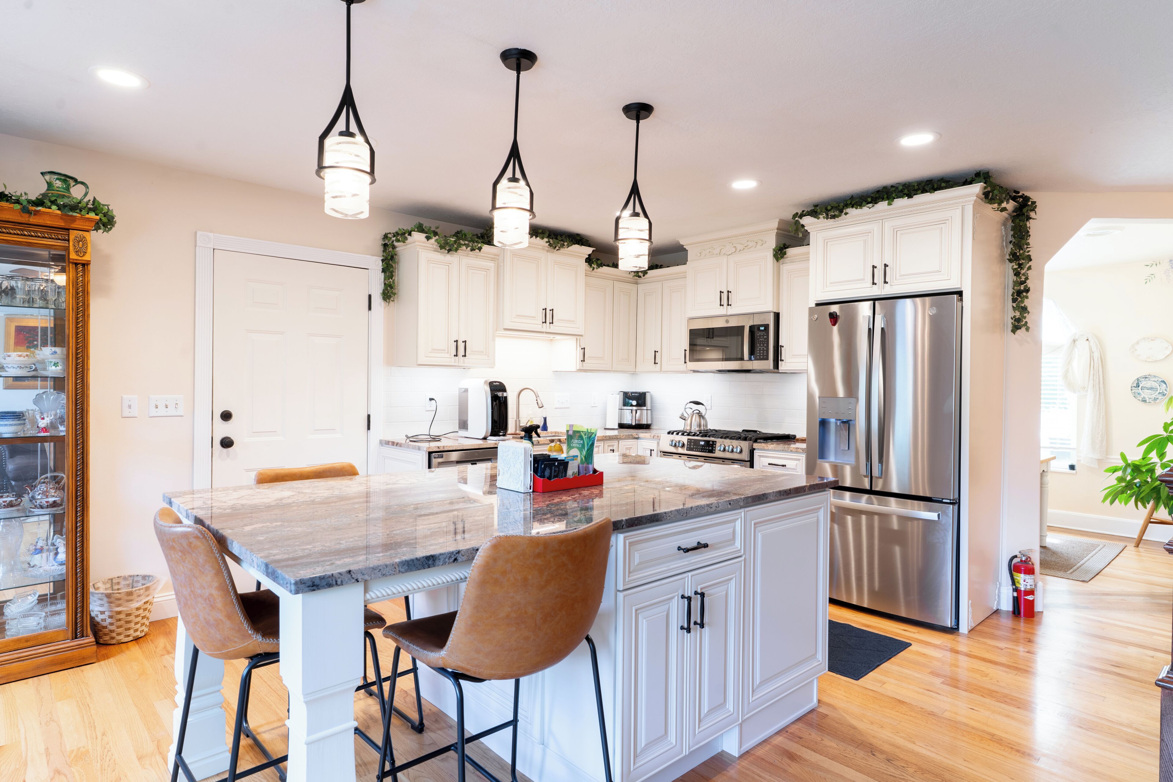 A modern kitchen with white cabinetry, a central island with bar stools, stainless steel appliances, and pendant lighting.