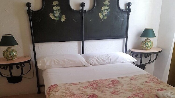 A bed with a floral bedspread, a dark headboard with floral decorations, two bedside tables with lamps, and a brick floor. - Residenza Villa Spagnola Adults Only (Parghelia)