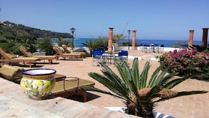 A sunlit outdoor seating area with lounge chairs and tables, overlooking a coastal landscape. - Residenza Villa Spagnola Adults Only (Parghelia)