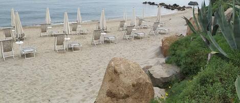 A beach with lounge chairs and umbrellas arranged for sunbathing.