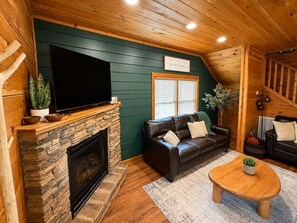 A cozy living room with a stone fireplace, leather sofas, a flat-screen TV, and a wooden ceiling. - The Overlook-Luxury Cabin Mtn View Walk to Parkway (Pigeon Forge)