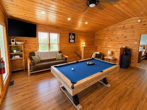 Ein gemütliches Zimmer mit Billardtisch, einer Couch und einem Deckenventilator.