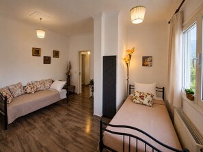 A room with two beds, a sitting area, a large window with a view, and a door leading to another room.