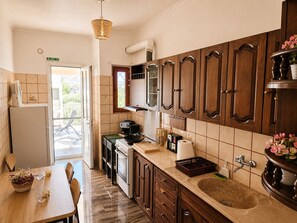 A kitchen with wooden cabinets, a sink, a stove, and a dining area with a table and chairs. - Aposperitis - Endless View (Amarinthos)
