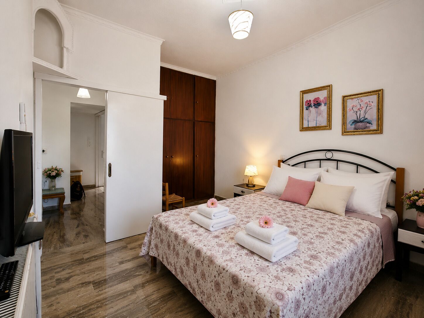 A hotel room with a bed, a desk with a computer, a wardrobe, and two paintings on the wall.