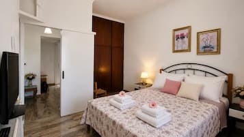 A hotel room with a bed, a desk with a computer, a wardrobe, and two paintings on the wall.