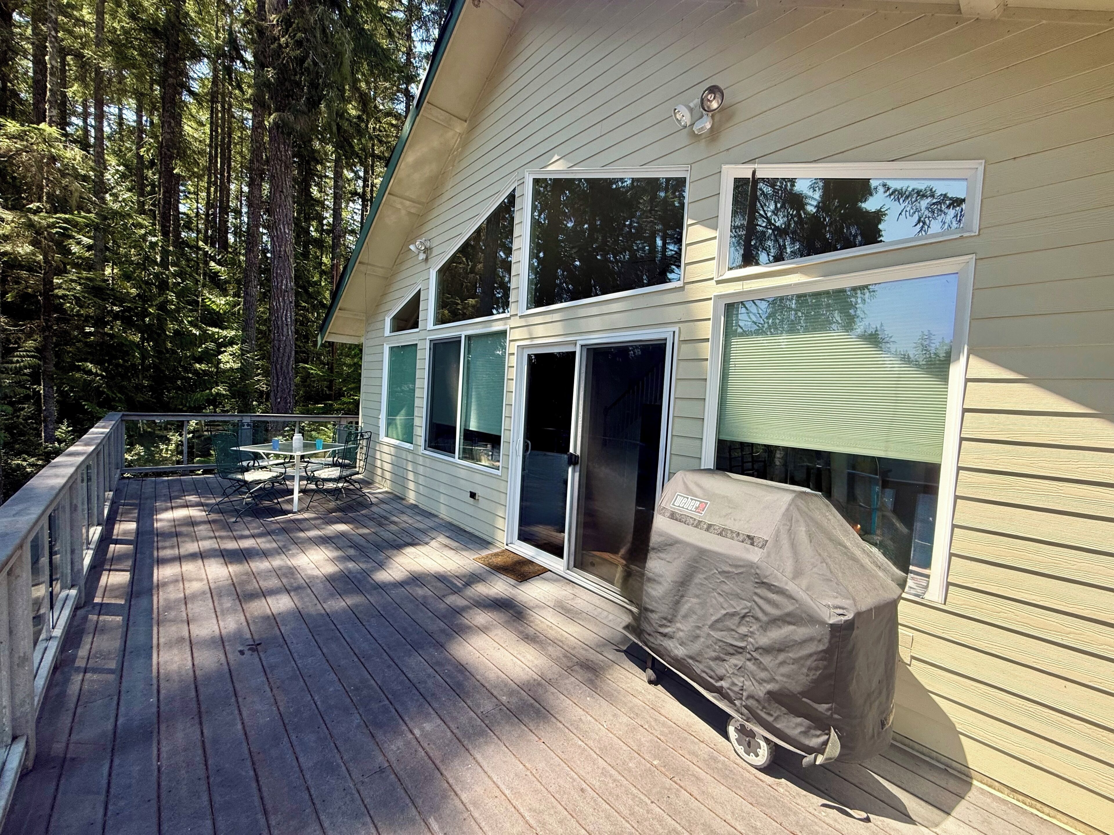 A deck with a table and chairs, a covered grill, and a house with large windows.