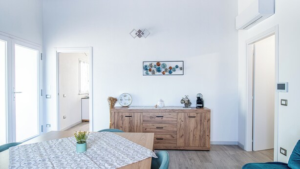 Moderni keittiö, jossa on puinen kaappi, kuvioidulla pöytäliinalla katettu ruokapöytä ja seinälle kiinnitetty kello.