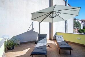 Eine Dachterrasse mit zwei Liegestühlen, einem großen Sonnenschirm und einem Blumentopf.