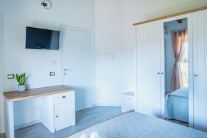 Ein Schlafzimmer mit einem Bett, einem an der Wand montierten Fernseher, einem Nachttisch und einem Kleiderschrank.