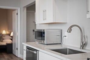 A modern kitchen with white cabinets, a microwave, a stainless steel sink, and a dishwasher. - Skyline Luxury - Stylish 1BR with Panoramic Views (Pittsburgh)
