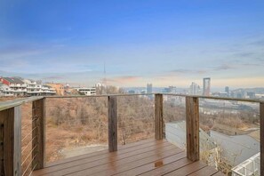 A wooden deck with a metal railing overlooking a cityscape with buildings and a clear sky. - Skyline Luxury - Stylish 1BR with Panoramic Views (Pittsburgh)