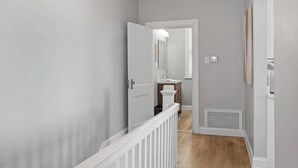 A hallway with a white door, a small bathroom with a sink and mirror, and a light switch on the wall. - Skyline Luxury - Stylish 1BR with Panoramic Views (Pittsburgh)