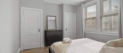Un dormitorio con cama, cómoda, espejo y ventana con persianas.