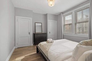 Een slaapkamer met een bed, een kastje, een spiegel en een raam met jaloezieën.
